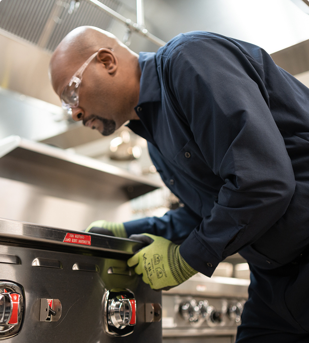 Service technician in a cap and work gloves inspecting commercial kitchen equipment up close