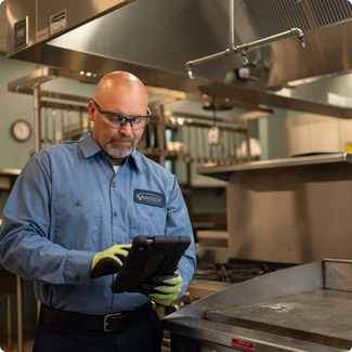 Service technician in safety glasses reviewing a tablet in a commercial kitchen