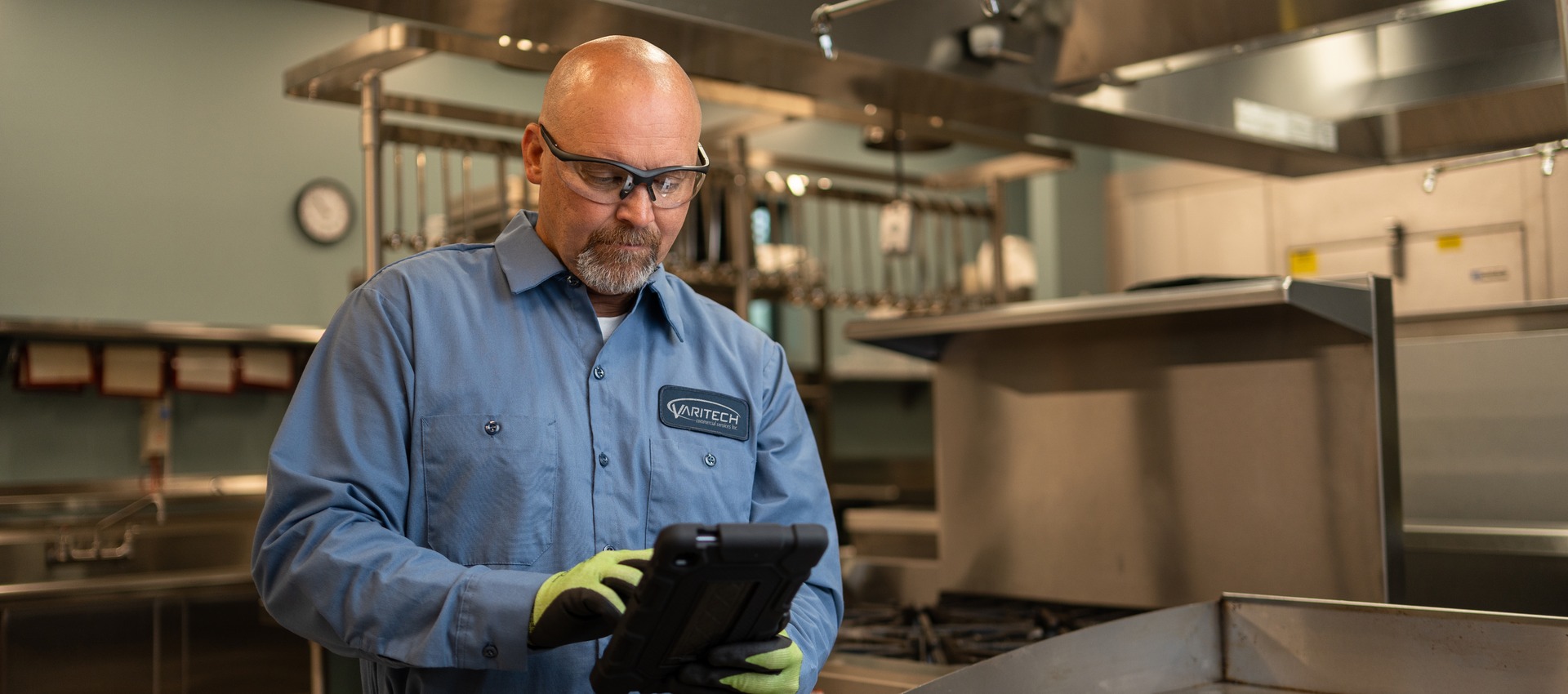 Service technician in safety glasses reviewing a tablet in a commercial kitchen