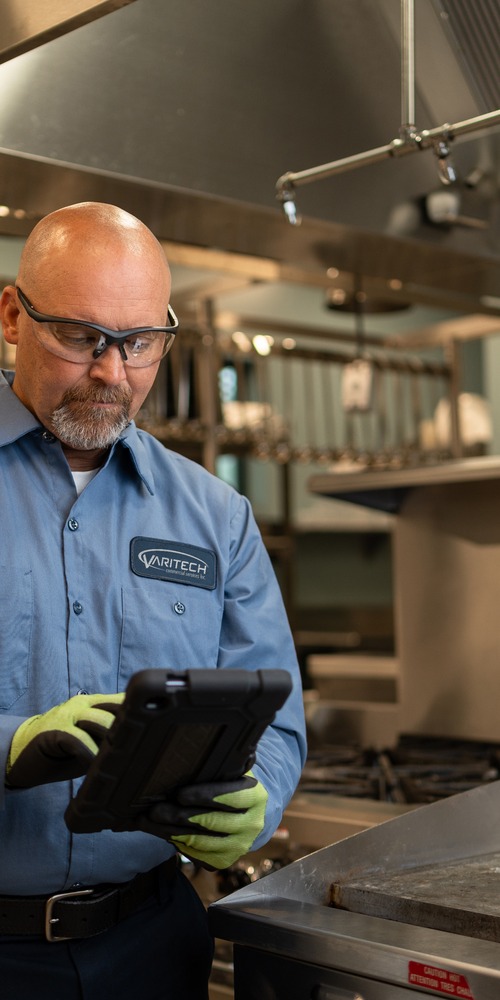 Service technician in safety glasses reviewing a tablet in a commercial kitchen