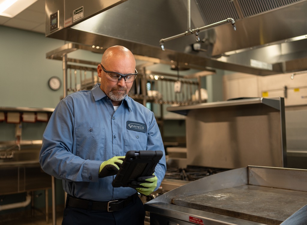 Service technician in safety glasses reviewing a tablet in a commercial kitchen