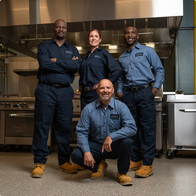 Team of four commercial kitchen service technicians in uniform posing together in a kitchen