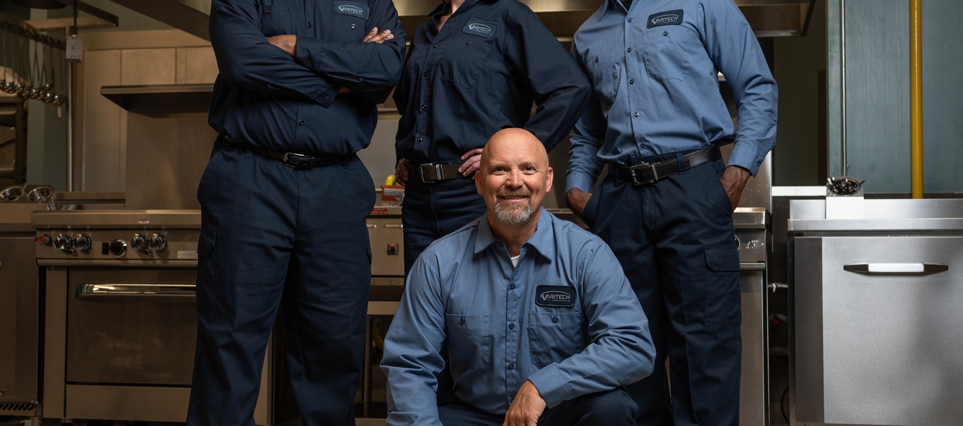 Team of four commercial kitchen service technicians in uniform posing together in a kitchen