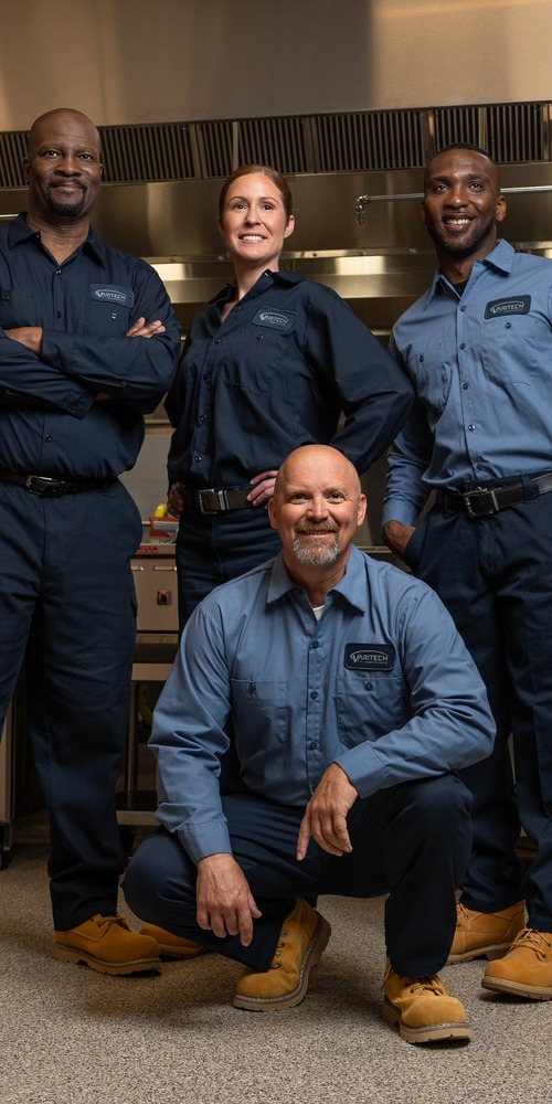 Team of four commercial kitchen service technicians in uniform posing together in a kitchen