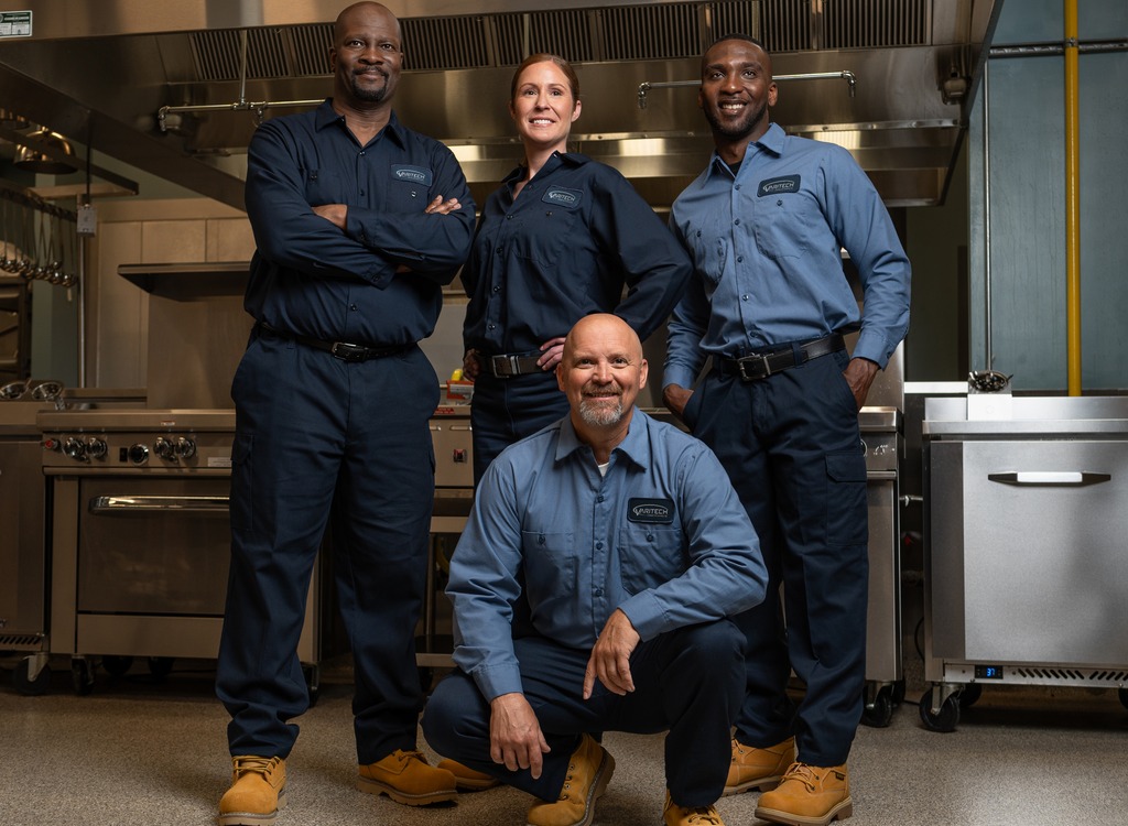 Team of four commercial kitchen service technicians in uniform posing together in a kitchen