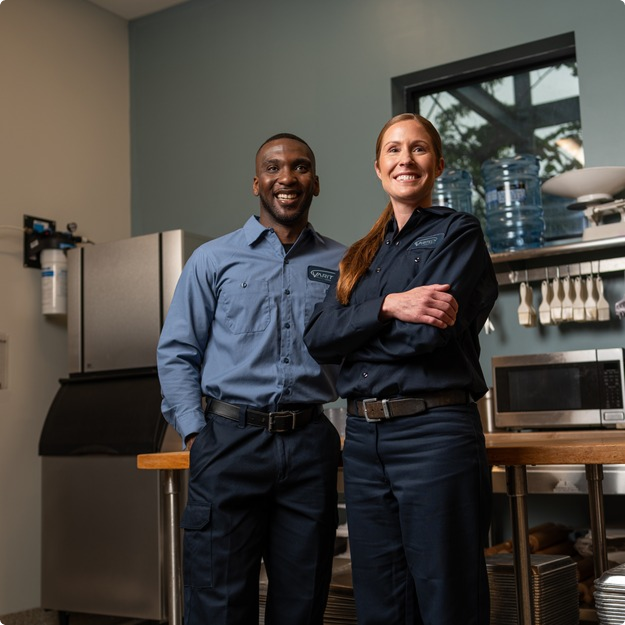 Two smiling commercial kitchen service technicians in uniform standing side by side
