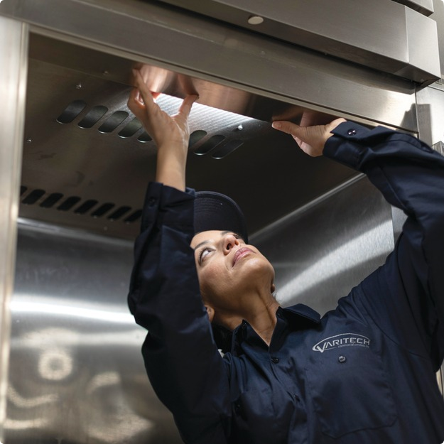 Service technician reaching overhead to inspect stainless steel commercial kitchen equipment