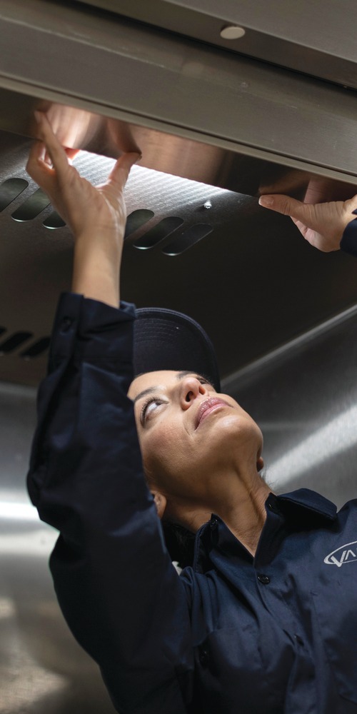 Service technician reaching overhead to inspect stainless steel commercial kitchen equipment