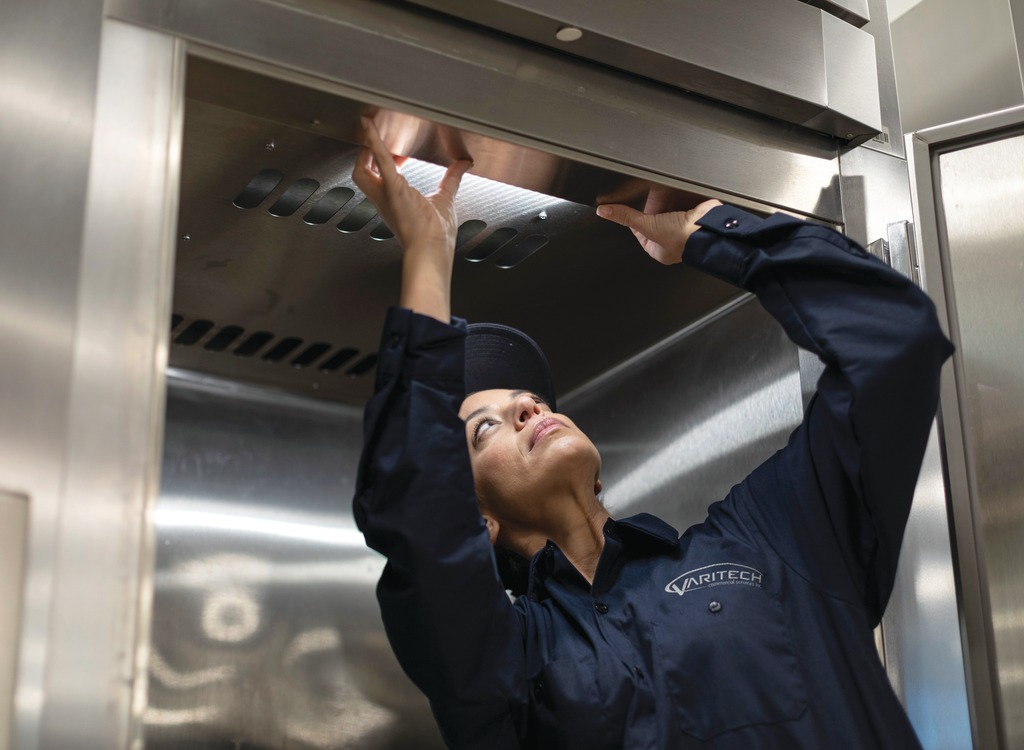 Service technician reaching overhead to inspect stainless steel commercial kitchen equipment