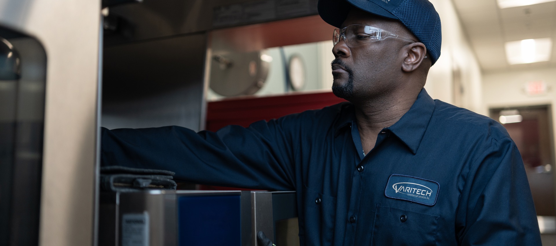 Service technician in a cap and safety glasses reaching into commercial kitchen equipment