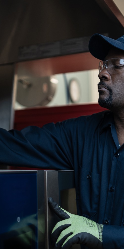 Service technician in a cap and safety glasses reaching into commercial kitchen equipment
