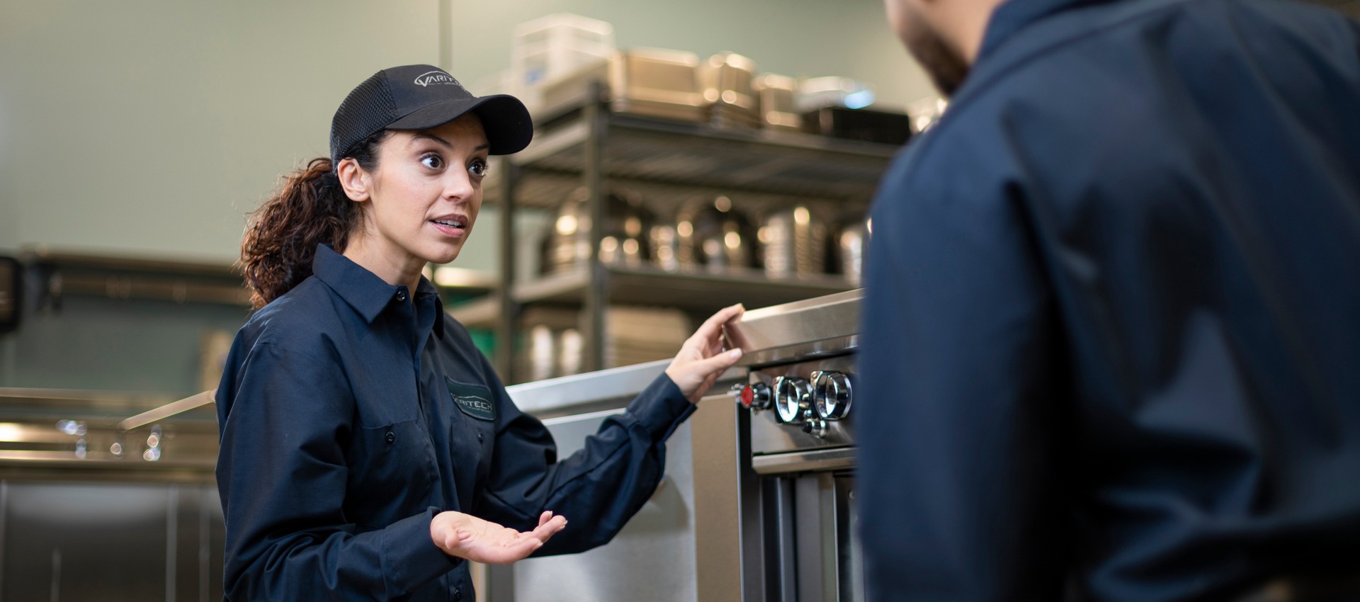 Service technician kneeling beside commercial kitchen equipment and talking with a colleague