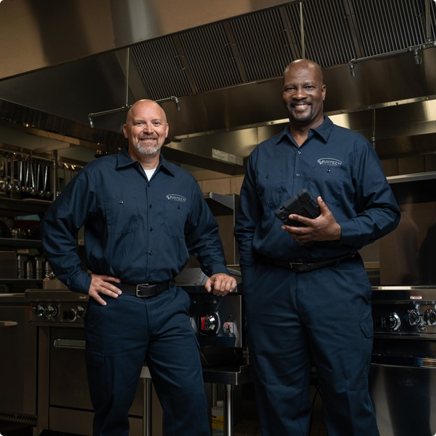 Two smiling service technicians in navy uniforms standing in a commercial kitchen
