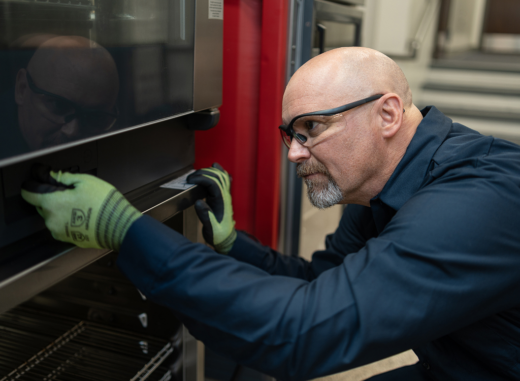 Service technician in safety glasses and work gloves working on a commercial oven door