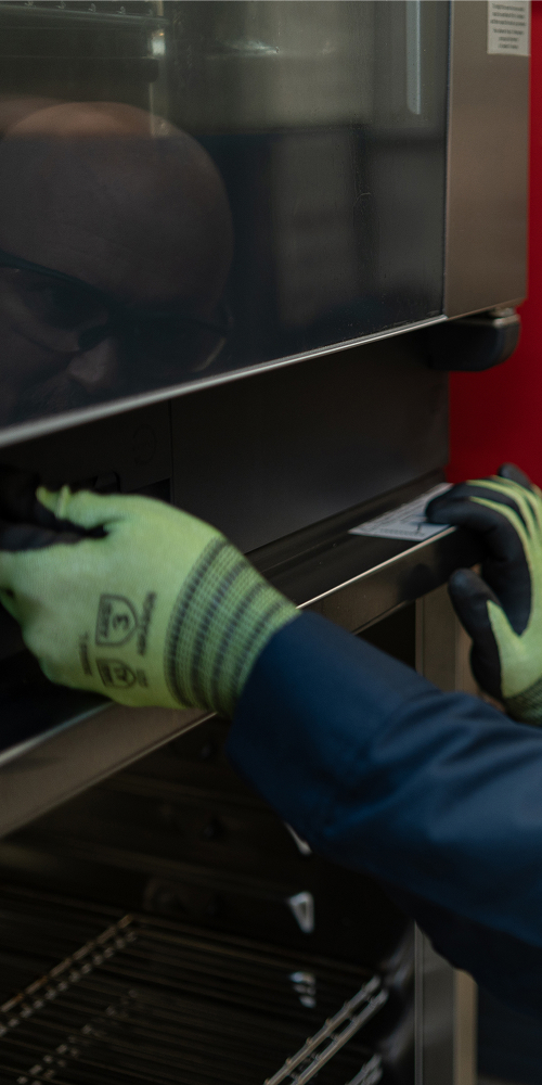 Service technician in safety glasses and work gloves working on a commercial oven door
