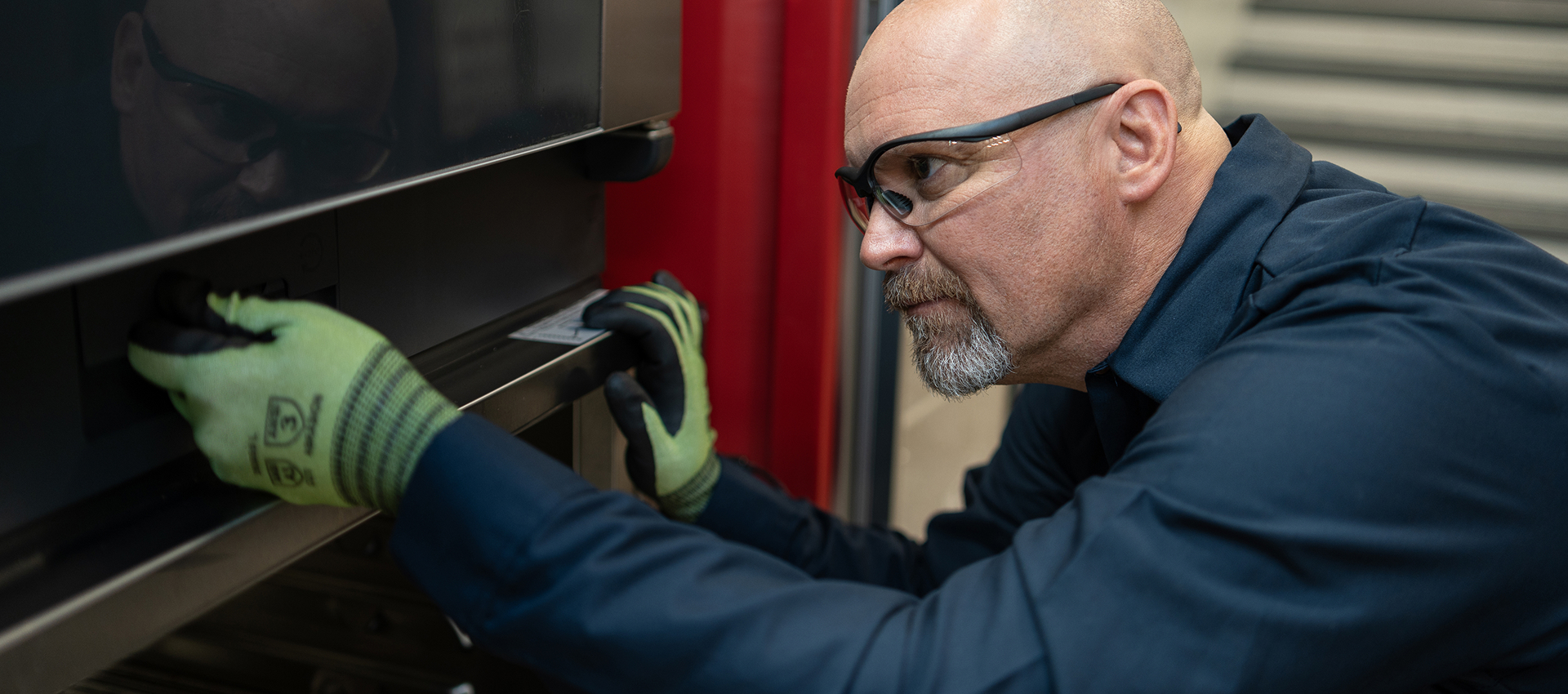 Service technician in safety glasses and work gloves working on a commercial oven door