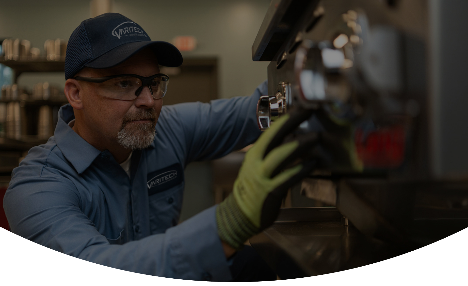 Service technician in a cap, safety glasses and work gloves repairing commercial kitchen equipment
