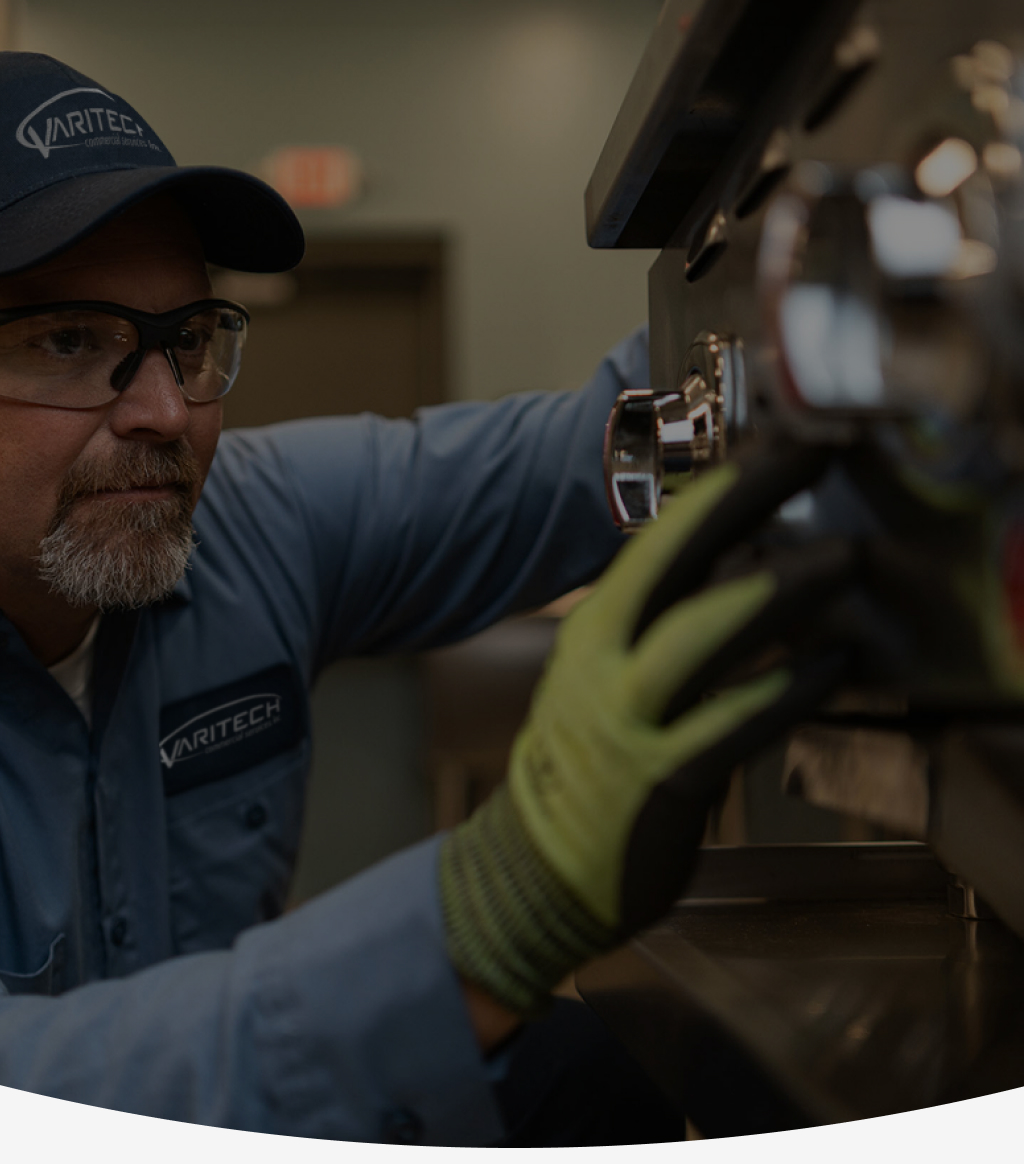Service technician in a cap, safety glasses and work gloves repairing commercial kitchen equipment