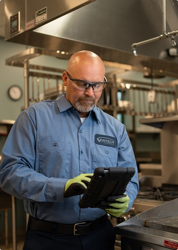Service technician in safety glasses reviewing a tablet in a commercial kitchen